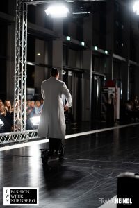 Markus in weißem zwei Reihen-Mantel (britischer Stil) mit E-Roller auf dem Laufsteg der Fashionweek Nürnberg von hinten - LikeMan Maßanzüge Nürnberg