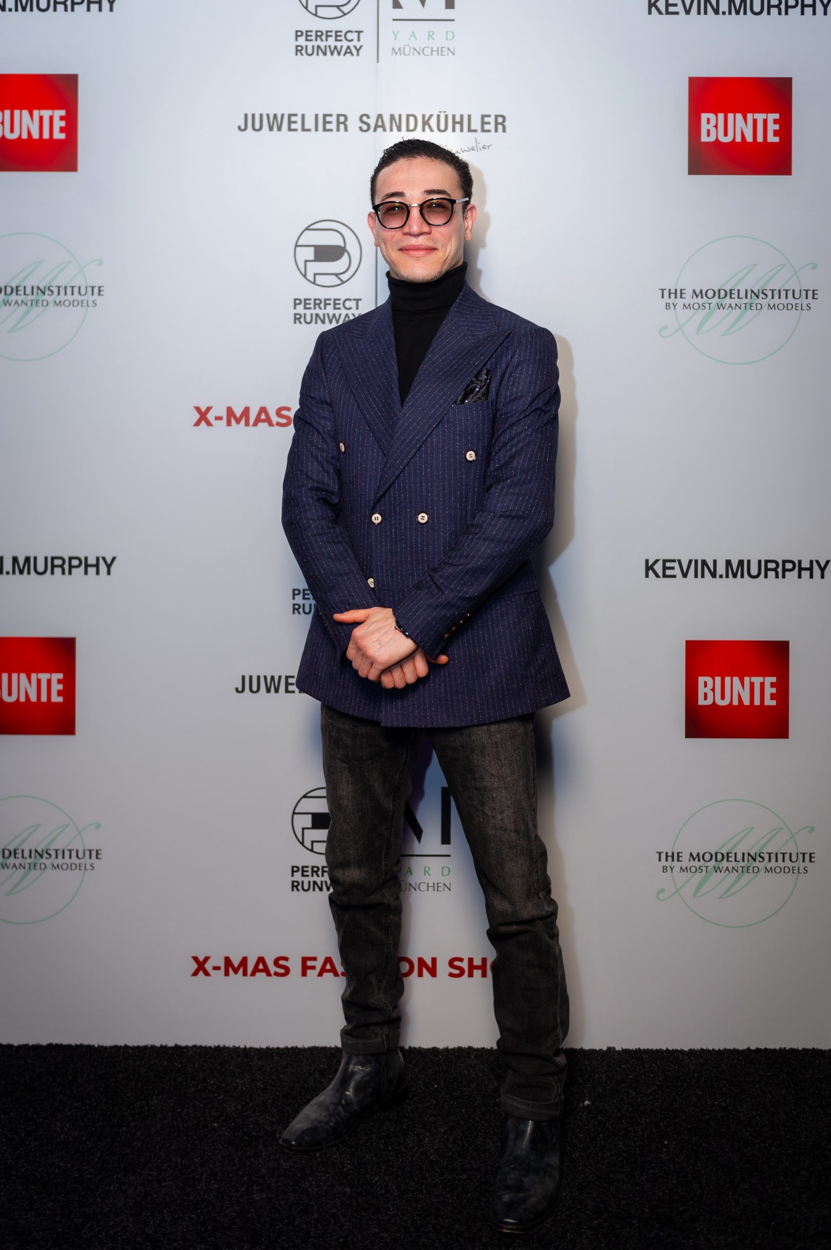 Morteza Faizi Designer auf der X-Mas Fashionweek München vor der Wand mit Blick in die Kamera- LikeMan Maßanzüge Nürnberg