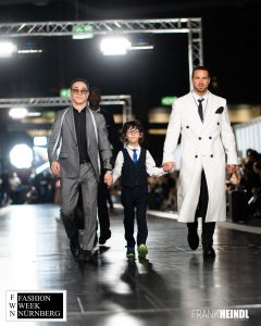 Morteza Faizi Designer mit Markus in weißem zwei Reihen-Mantel (britischer Stil) auf dem Laufsteg der Fashionweek Nürnberg mit Kind - LikeMan Maßanzüge Nürnberg